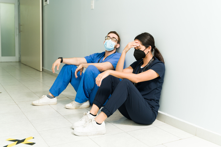 Two medical professionals looking exhausted while sitting on the floor. 