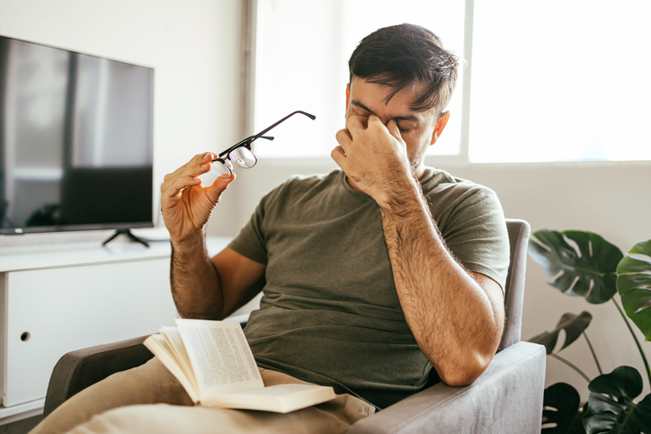 Tired man experiencing a migraine taking off his glasses and pinching his nose.