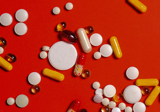 Collection of scattered pills in various sizes on top of a red background