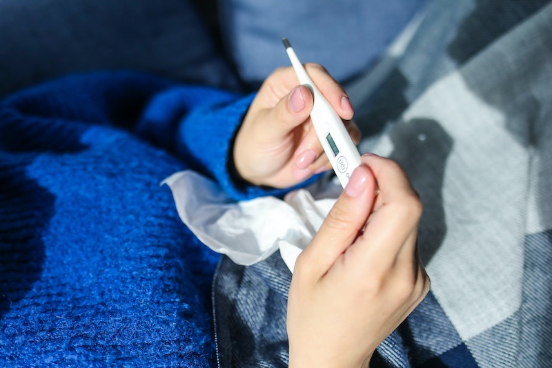 Woman in a blue sweater looking at a thermometer with a tissue on her lap.